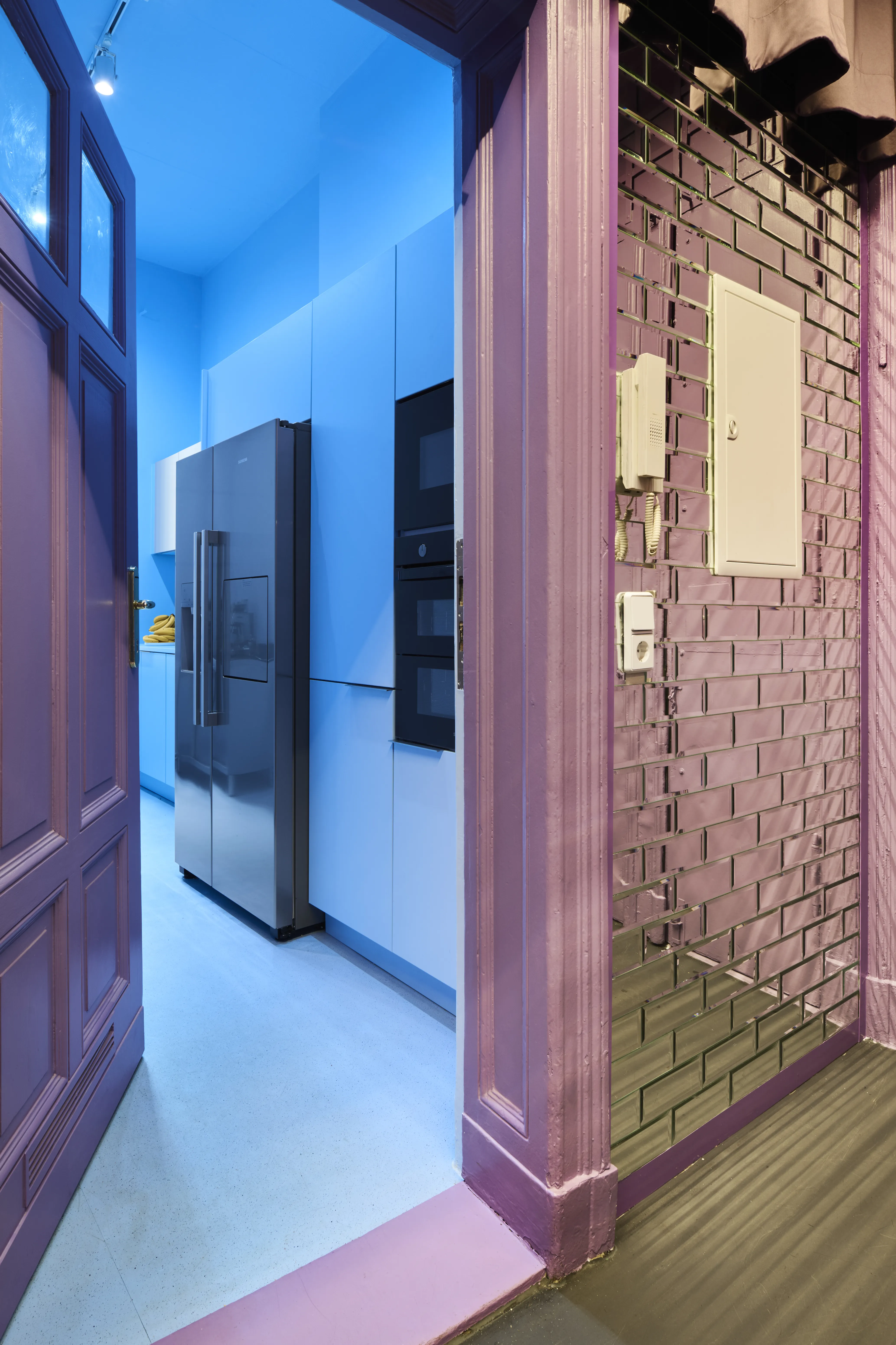 Lilac doorway with mirror tile wall leading into the light blue kitchen with built-in appliances.