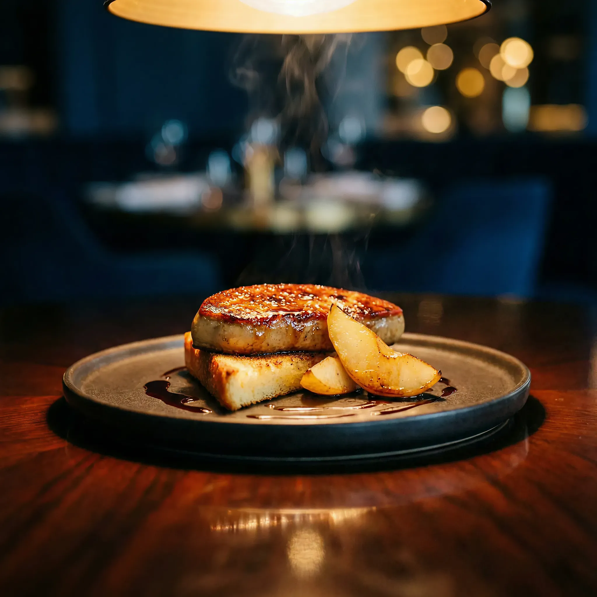 Seared foie gras with caramelized pear slices on toasted bread, drizzled with sauce, on a dark plate. Warm lighting creates an elegant, upscale ambiance.