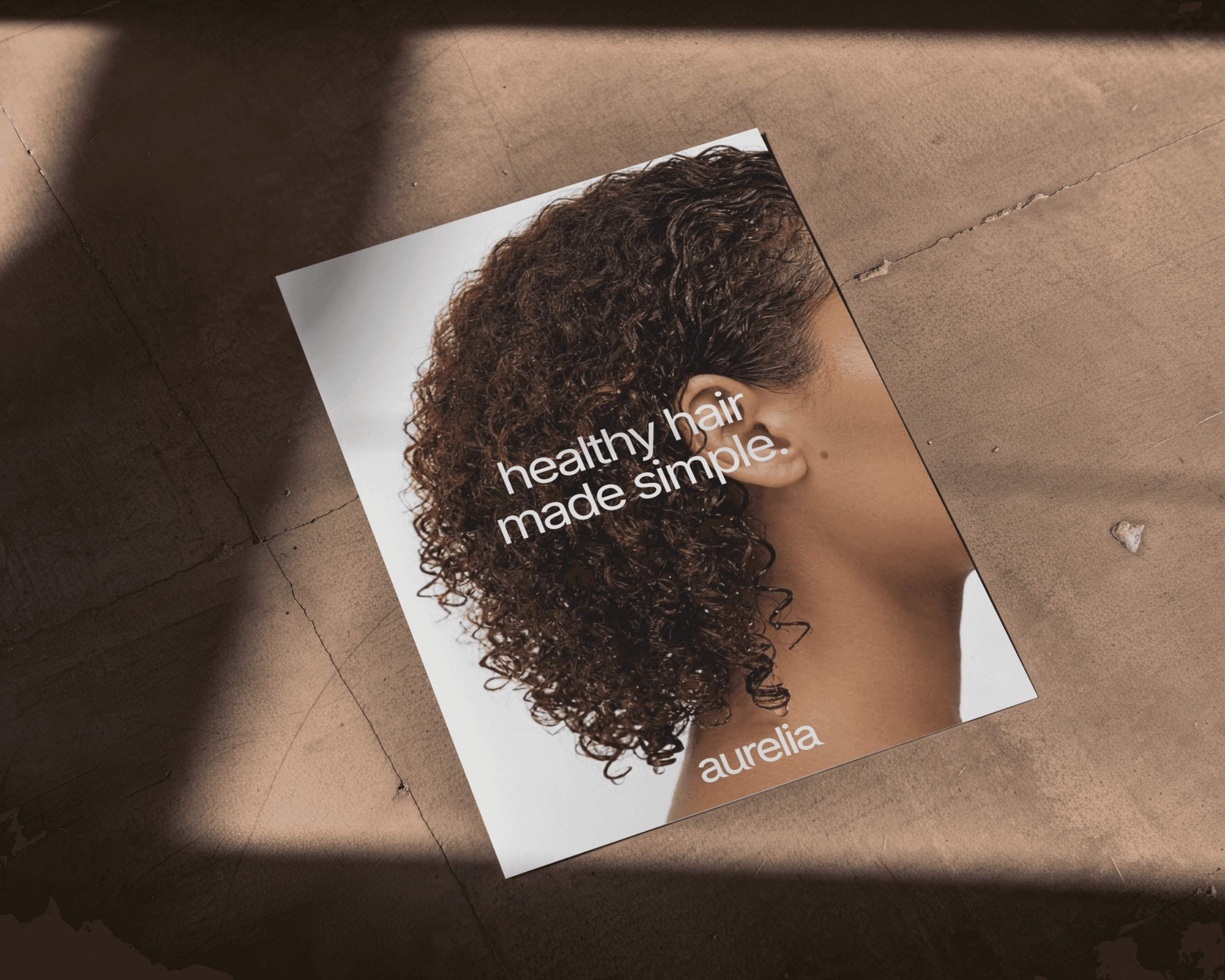 A poster for a haircare brand laying on the ground. The poster shows a woman with curly hair. The following text is featured on the poster: Healthy hair made simple.
