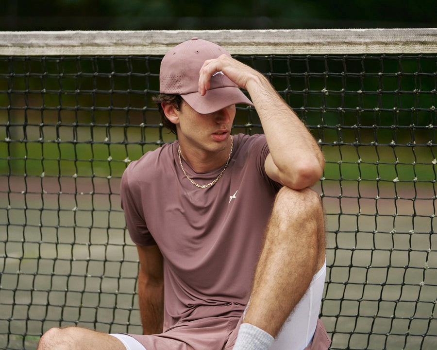 Tennis player in a muted rose Sigrún kit seated beside a tennis net.