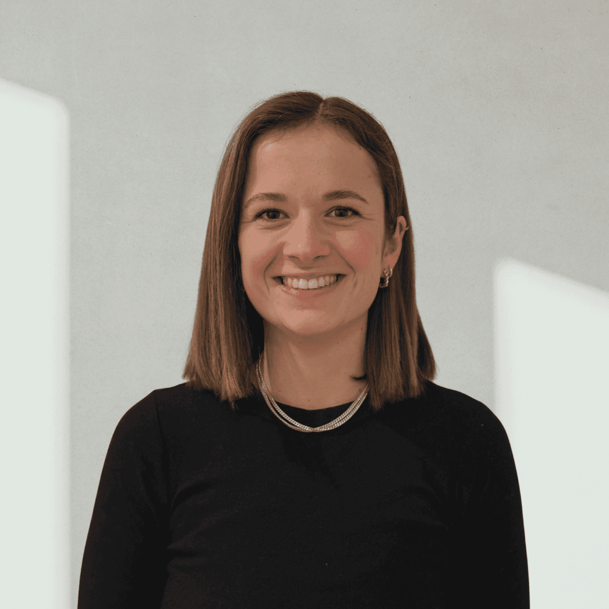 A smiling person with curly hair sits at a desk, looking at a laptop against a dark background.