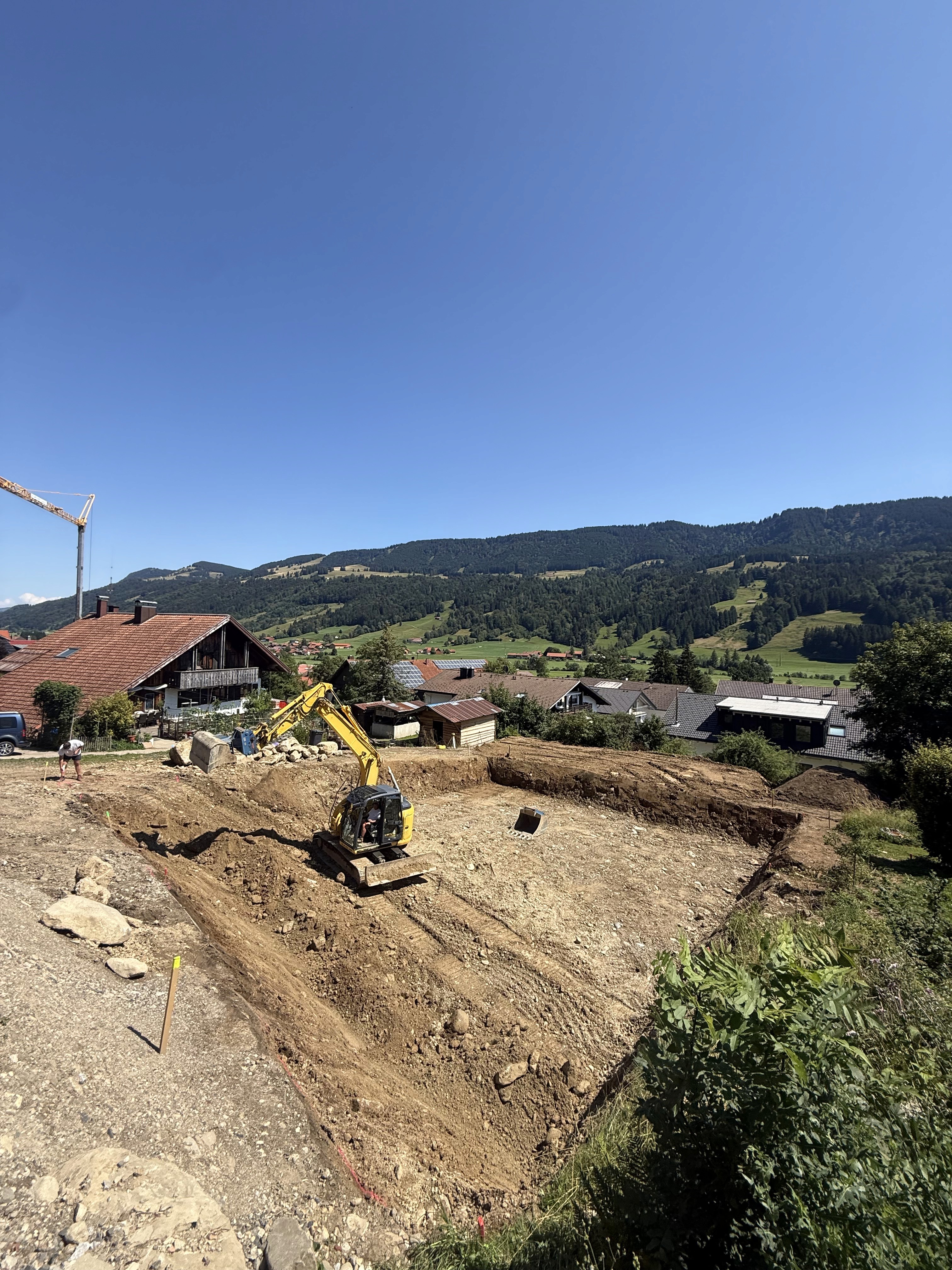 Ausgehobene Baugrube für sechs Neubauwohnungen in Oberstaufen mit Bagger in Hanglage
