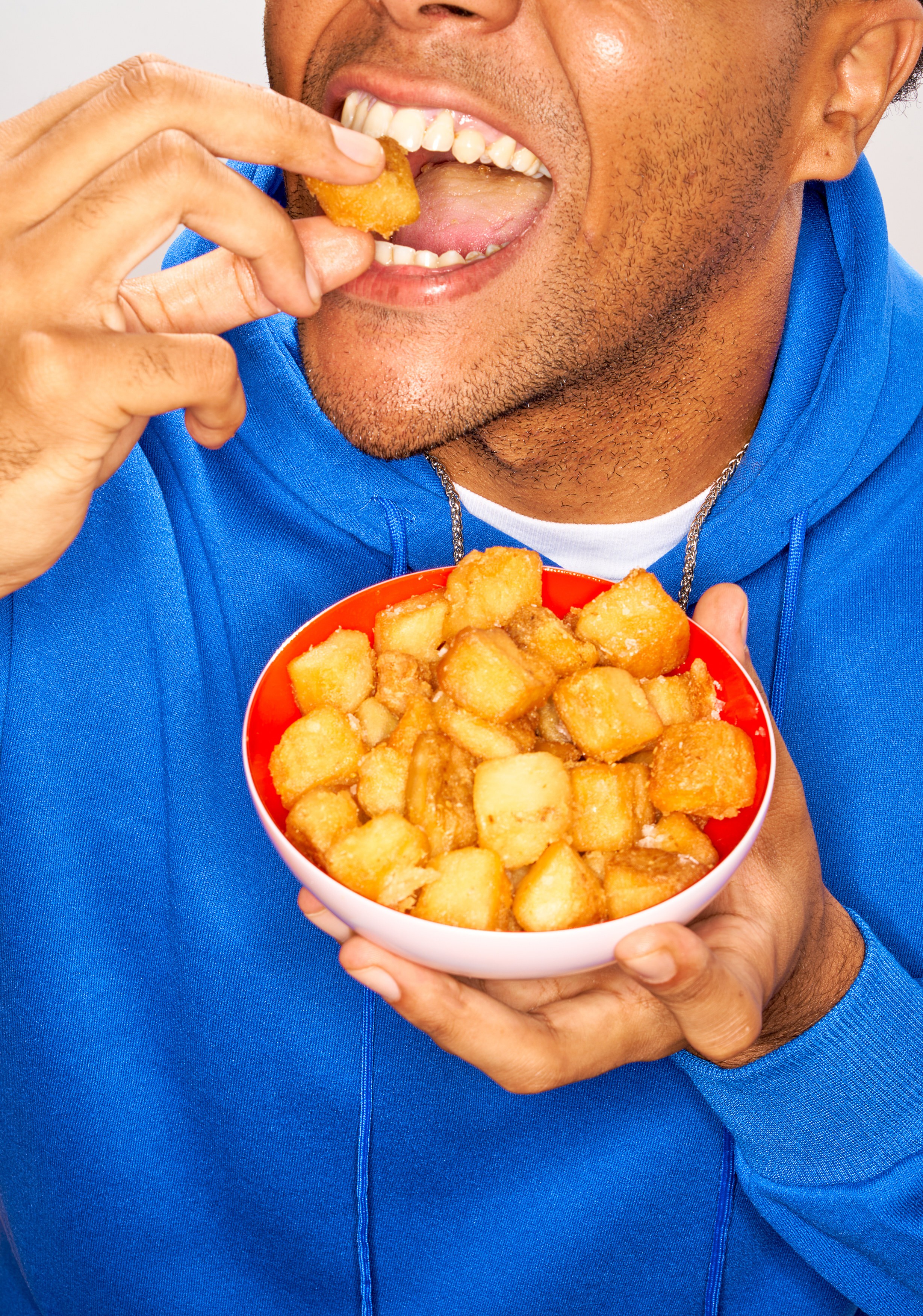 Talent in a bright blue sweatshirt eating crispy potatoes from a red bowl