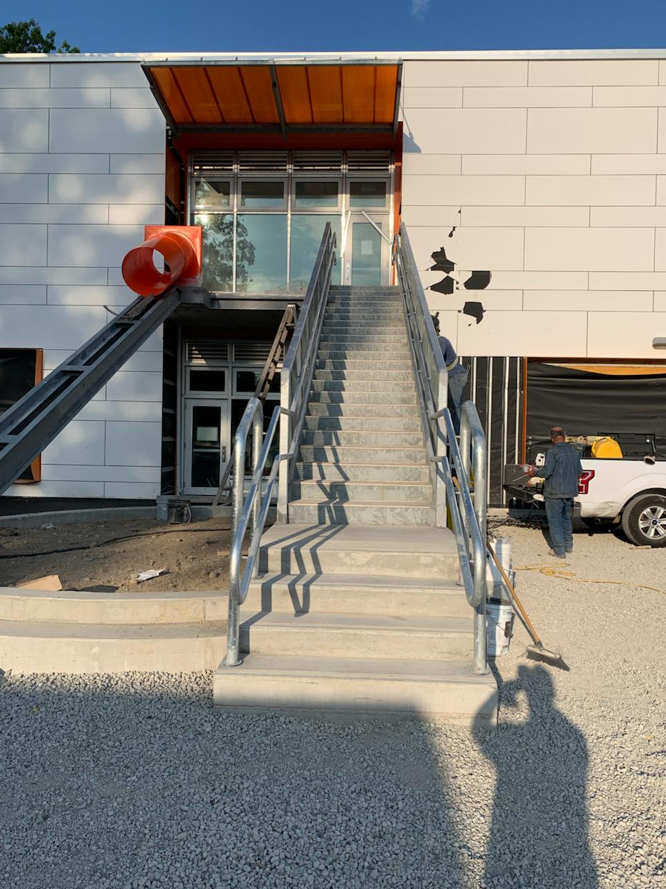 Galvanized entrance staircase and handrails beside orange building trim