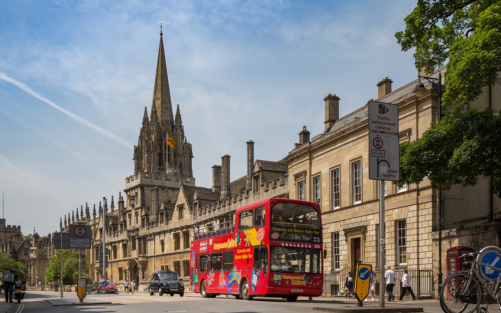Open-top tour bus passing historic Oxford architecture.