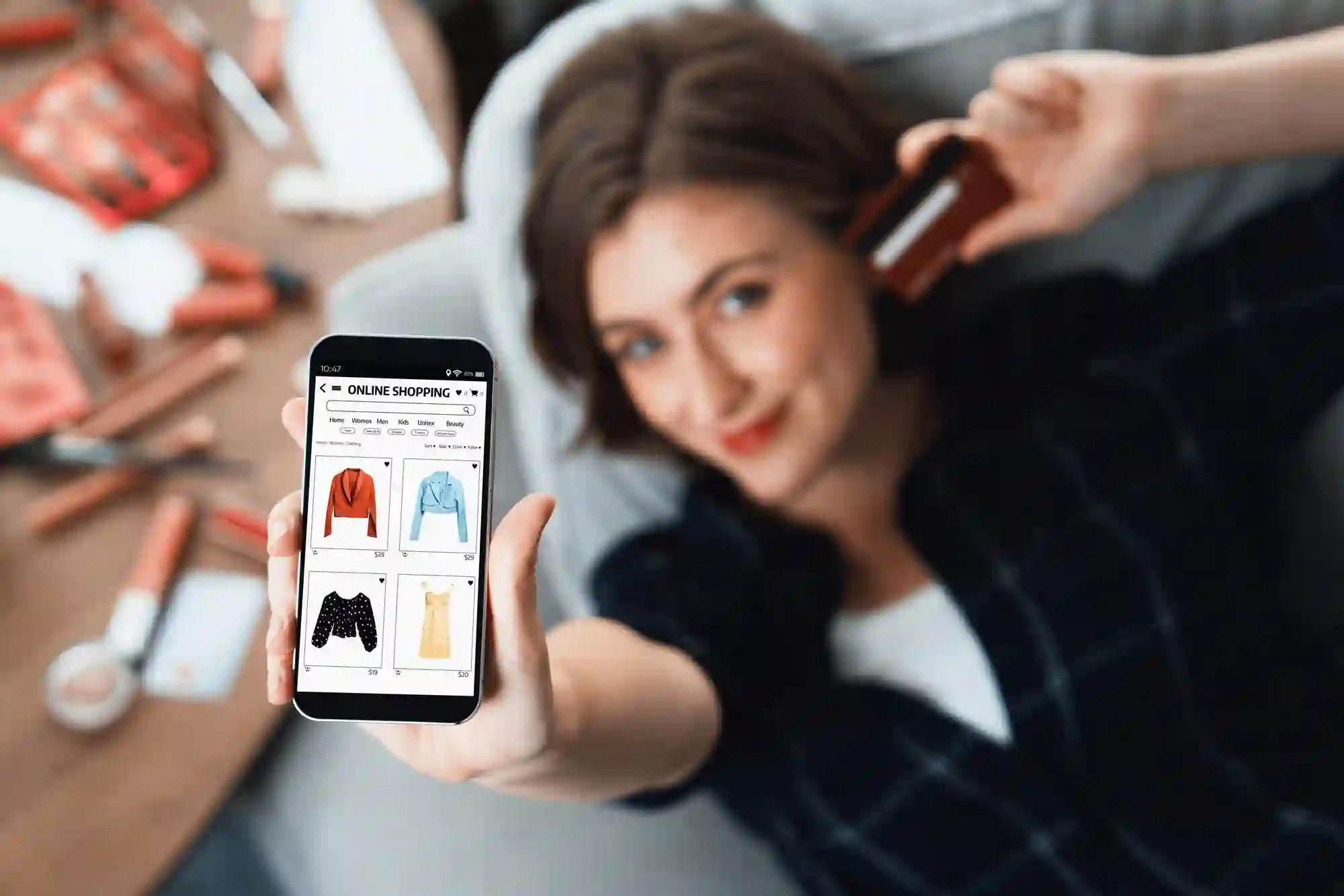 Woman holds up her phone displaying an online clothing store while holding a credit card, ready to shop.