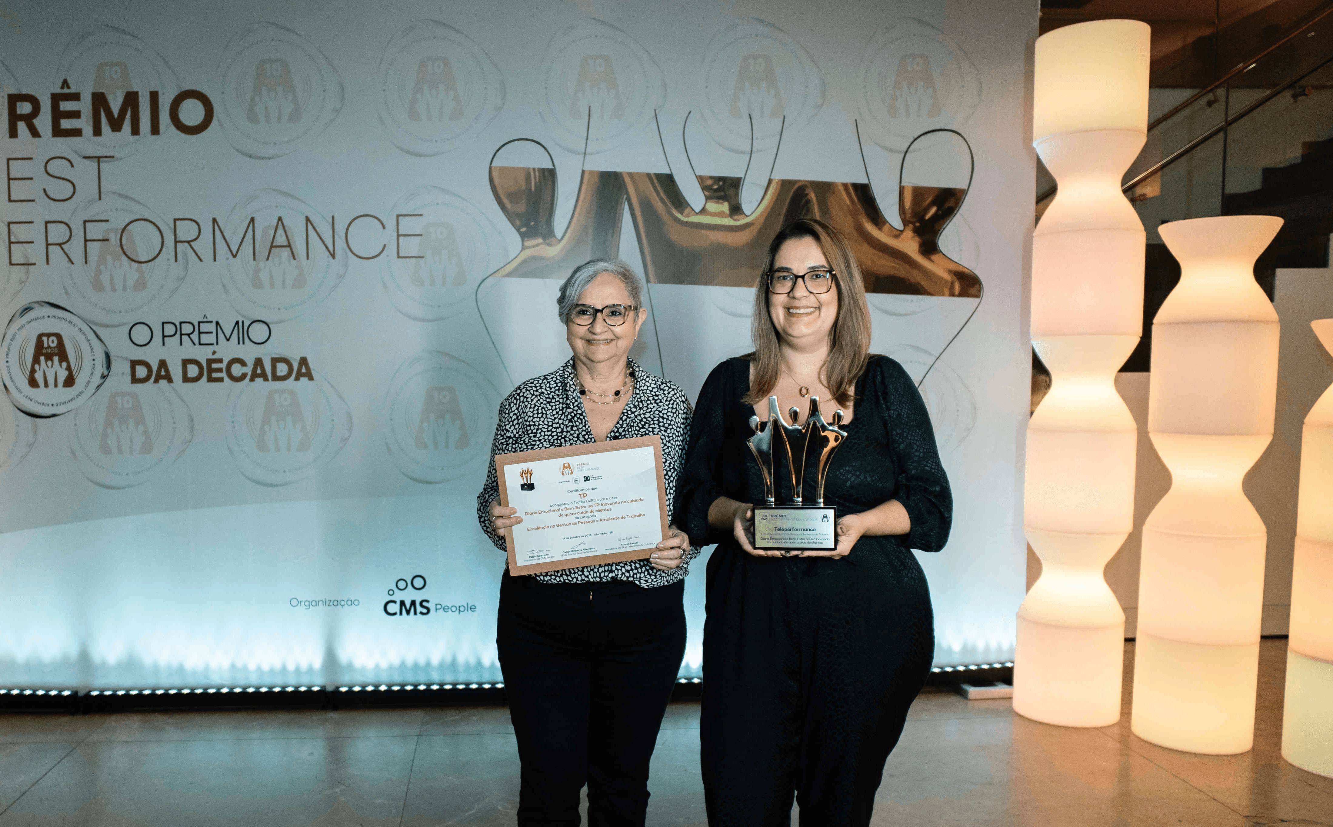 Executivos da TP posando com troféu ouro e certificado no palco do Prêmio Best Performance 2025
