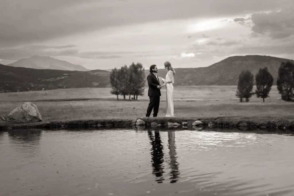 Black-and-white portrait of newlyweds beside a pond