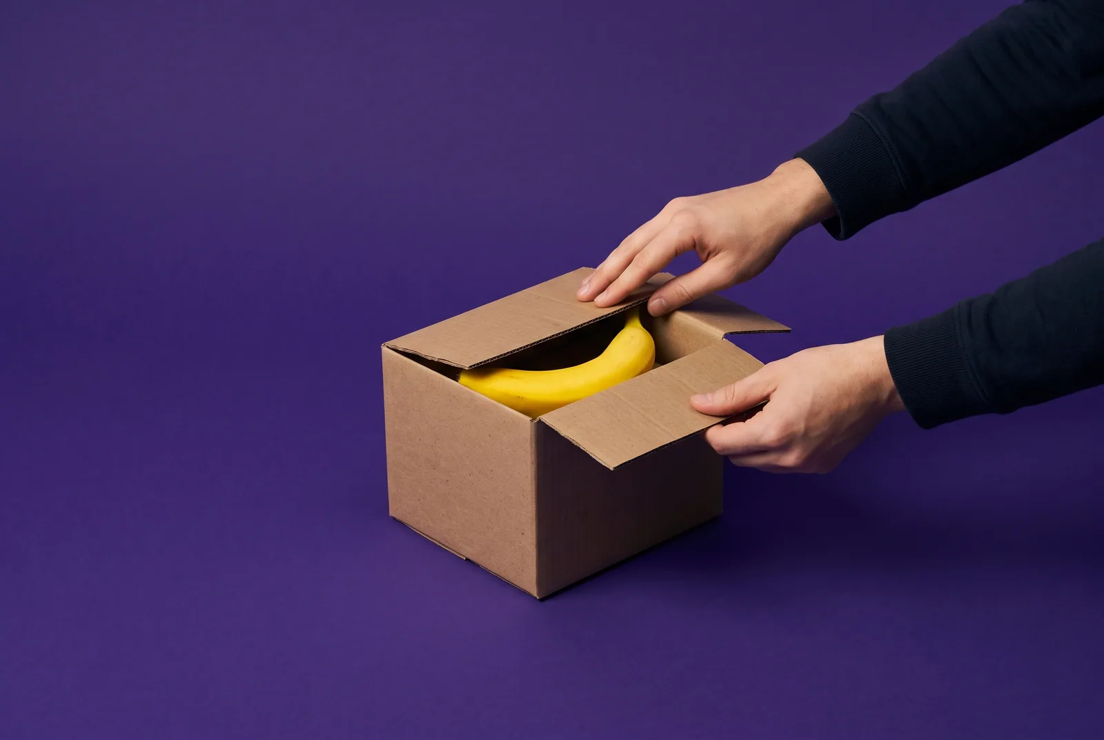 Hands closing a small moving box with a banana inside, a playful image for the best Remojo alternatives