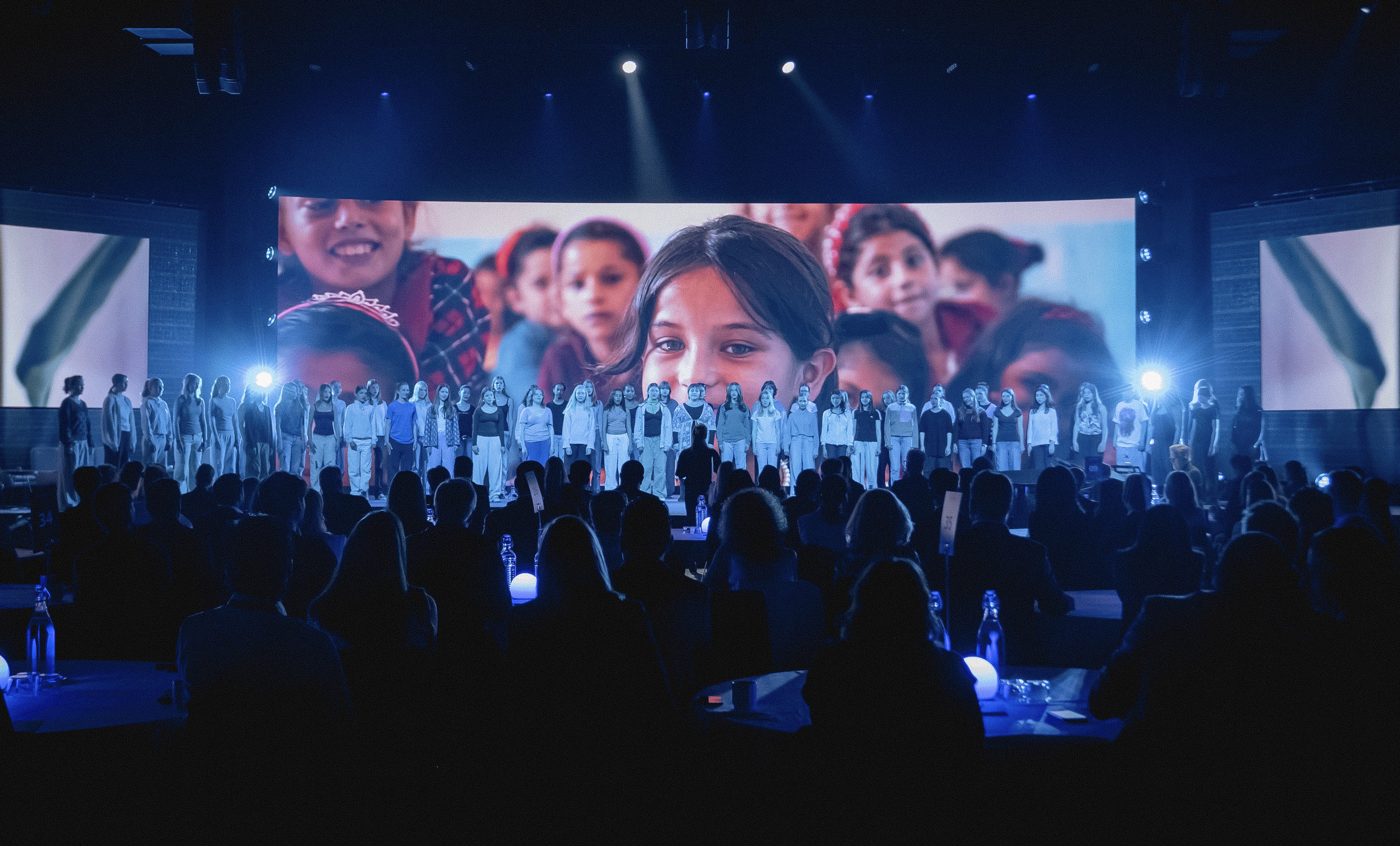 Barn som står på en scen framför en stor skärm