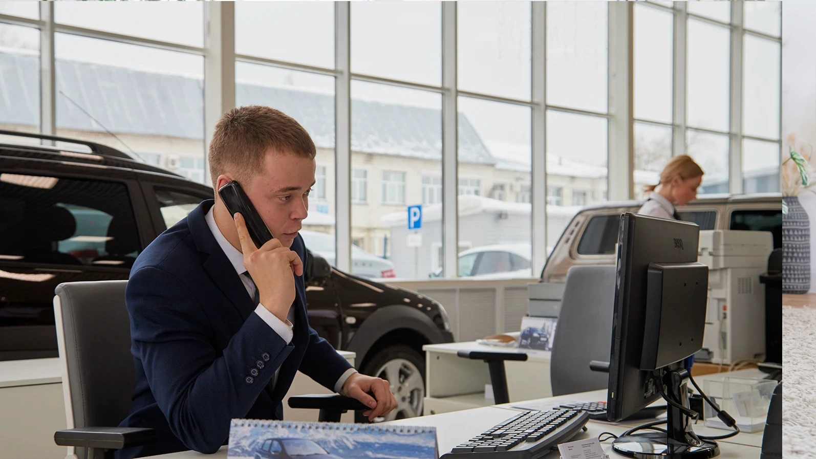 Kirov, Russia - February 26: Handsome male Manager in a suit with phone in showroom of dealership Autovaz and car Lada in Kirov city in 2019