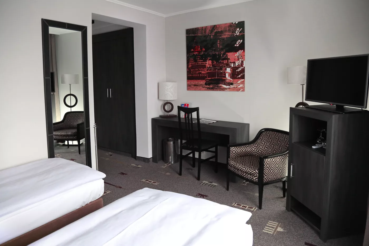 Bild von einem Zimmer mit zwei Einzelbetten mit Blick auf Schreibtisch, TV und Gemälde