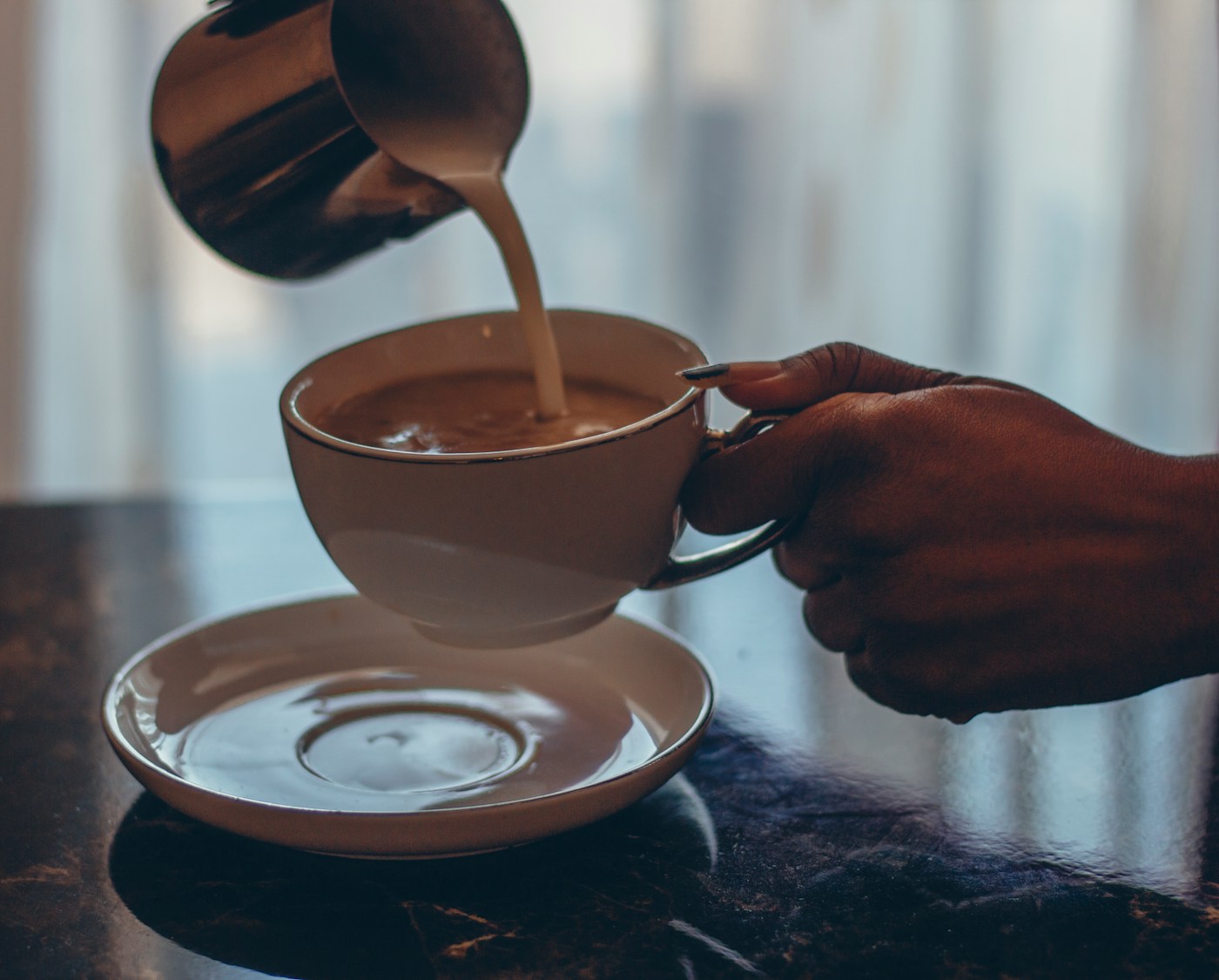 A hand pouring milk into a cup of coffee, illustrating how a food intolerance can be dose-dependent unlike an allergy