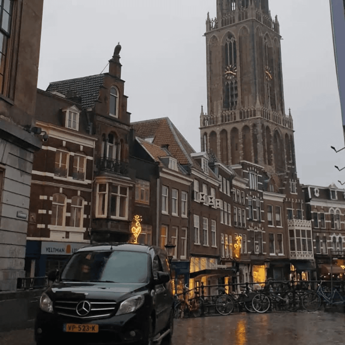Zwarte Van Ede Koeriers bus op weg voor stadsdistributie langs historische grachtenpanden en de domtoren