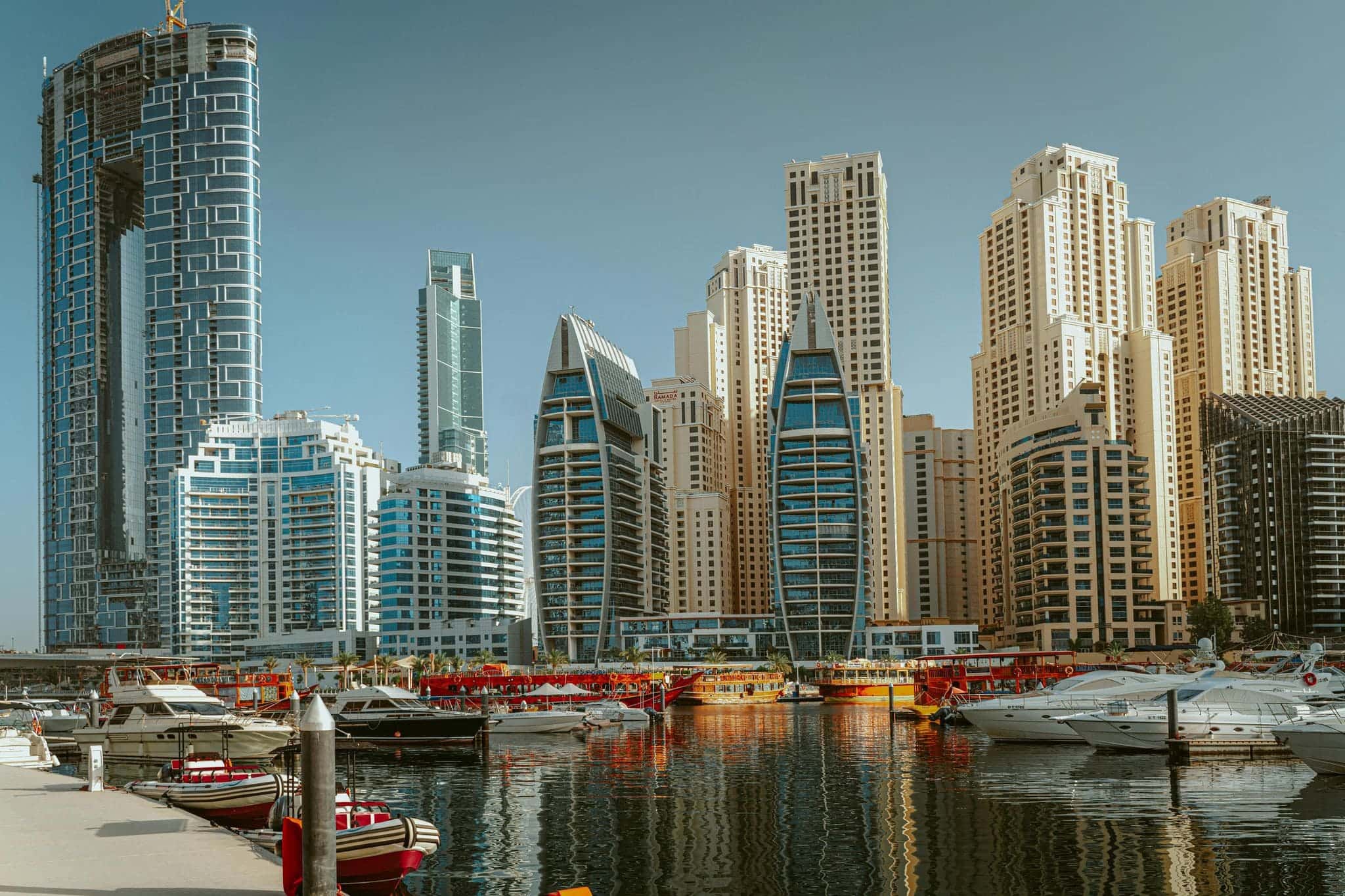 Daytime view of Dubai Marina with modern high-rise towers and boats docked along the waterfront.