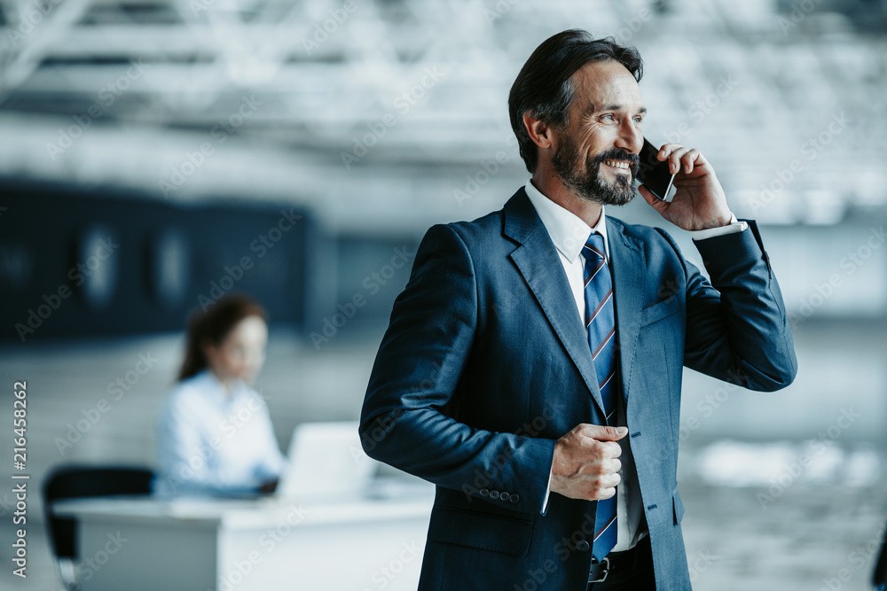 A businessman wearing a suit talks on the phone and is smiling