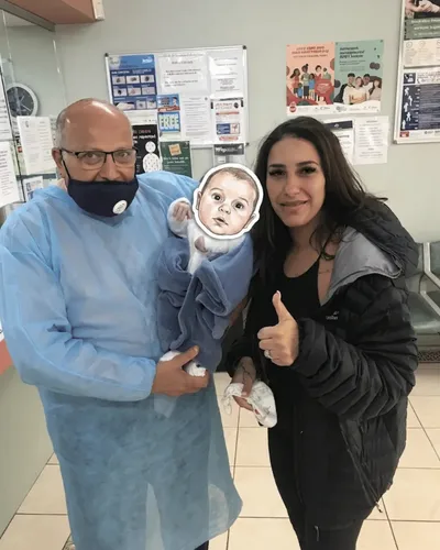Dr. Ashraf Saddik holding a swaddled newborn infant alongside a smiling mother at his Coburg clinic.