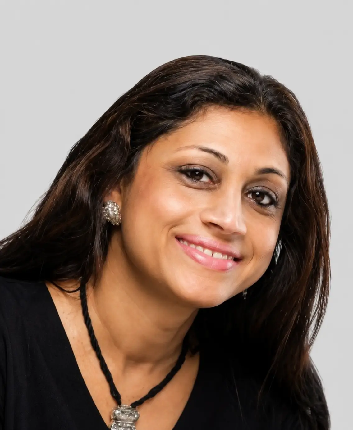 Portrait of a smiling woman with dark hair and a black necklace on a neutral background.