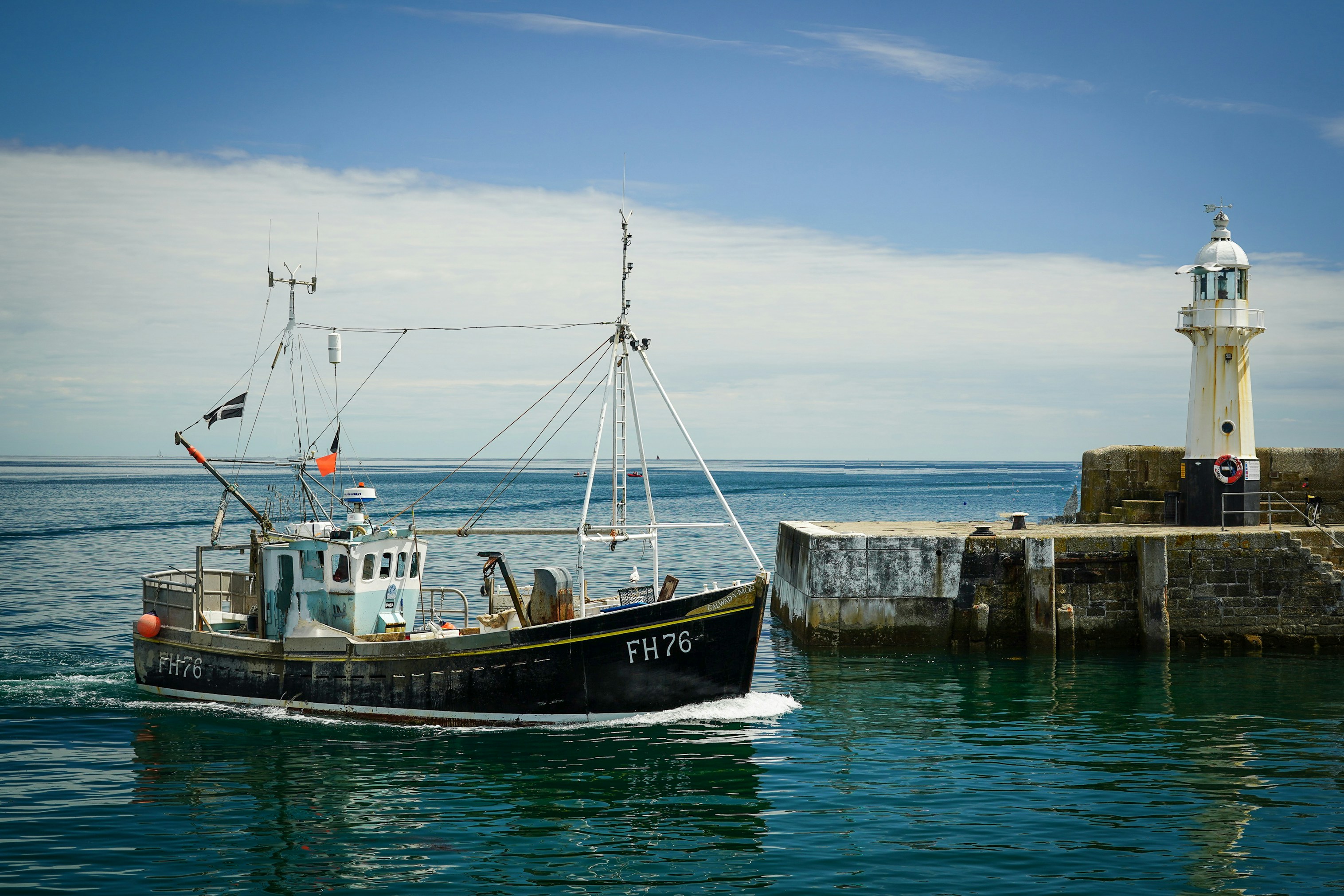 Fishing boat sailing past a lighthouse on a sunny day. Blue water and sky.