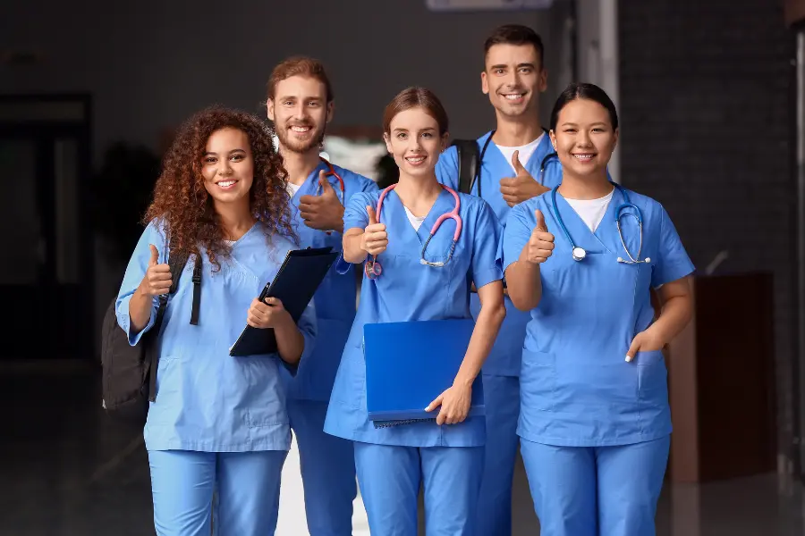 AI and medicine embraced by diverse group of smiling healthcare students giving thumbs up in scrubs.