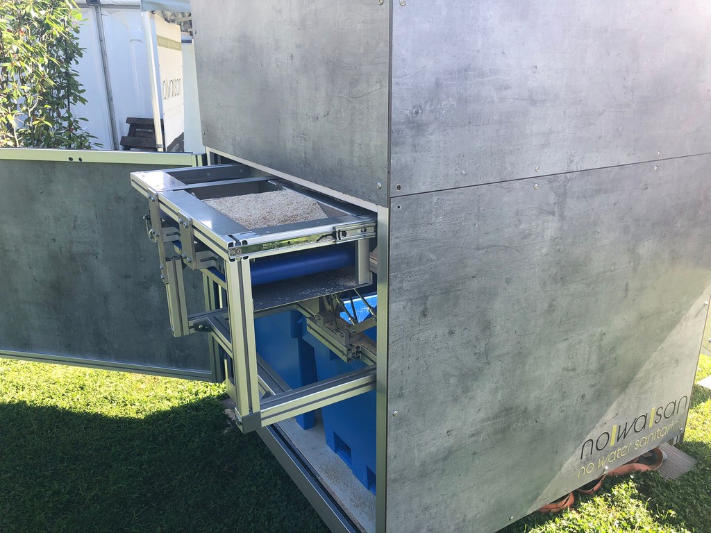 Detailfotoen vun der Technik hannert der NoWaSan dréchen Toilette – weist d'innere Mechanismen a Komponenten fir déi waasserlos Funktioun an nohalteg Entsuergung.