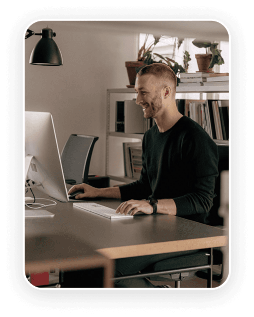 A person working on a computer desk, smiling, in a modern, minimalistic office environment.