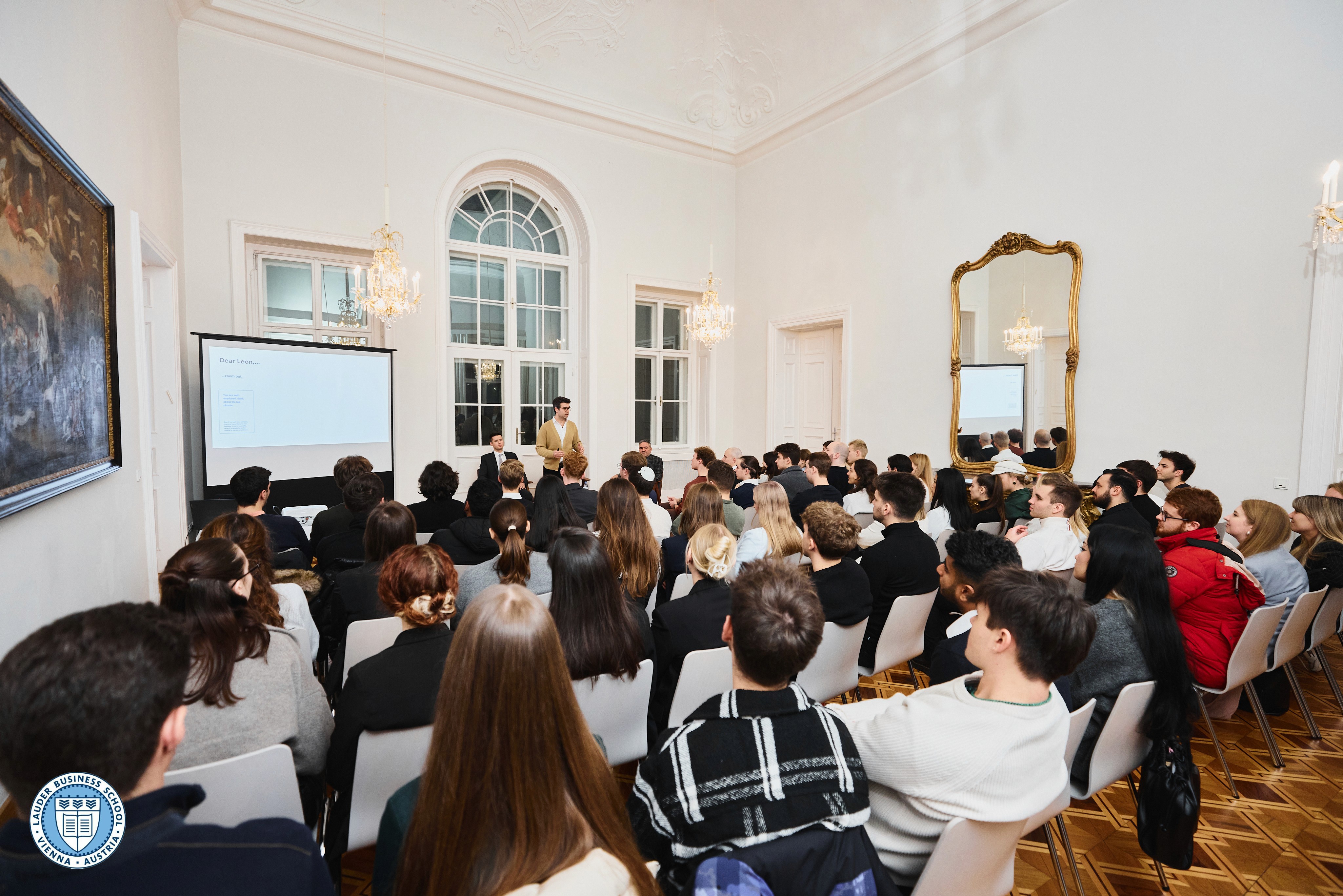 Group of LBS students sitting together, smiling and discussing while using a laptop in a modern campus setting