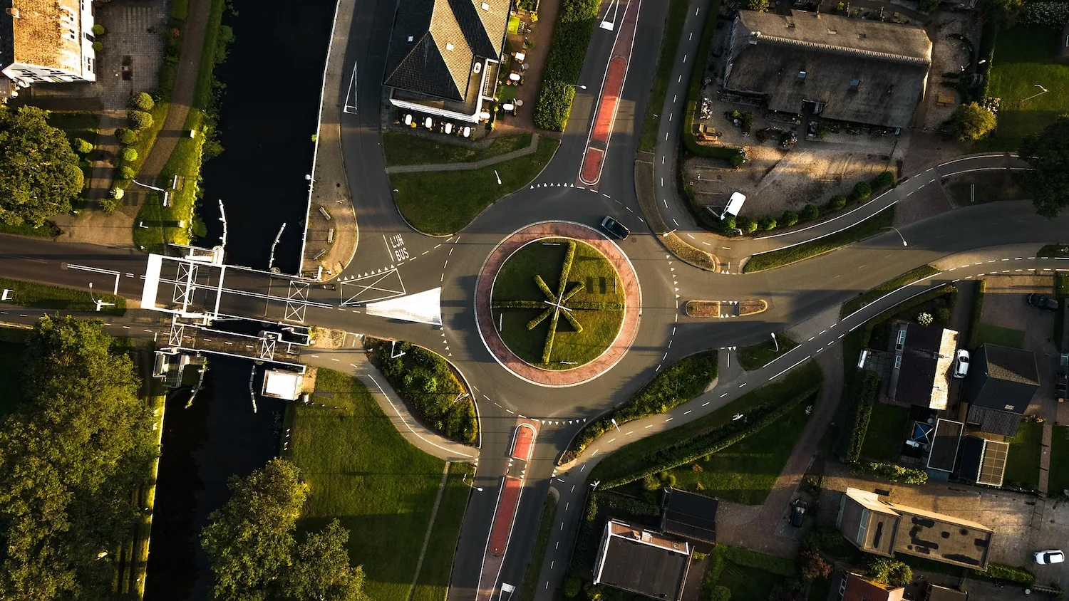 Scenic top-down drone photography capturing a roundabout with a unique star-shaped hedge and adjacent canal bridge.