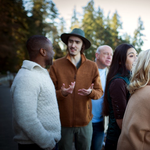 קבוצה של אנשים בחוץ, לבושים באופן לא רשמי, משוחחים ומחייכים, עם עצים ברקע.