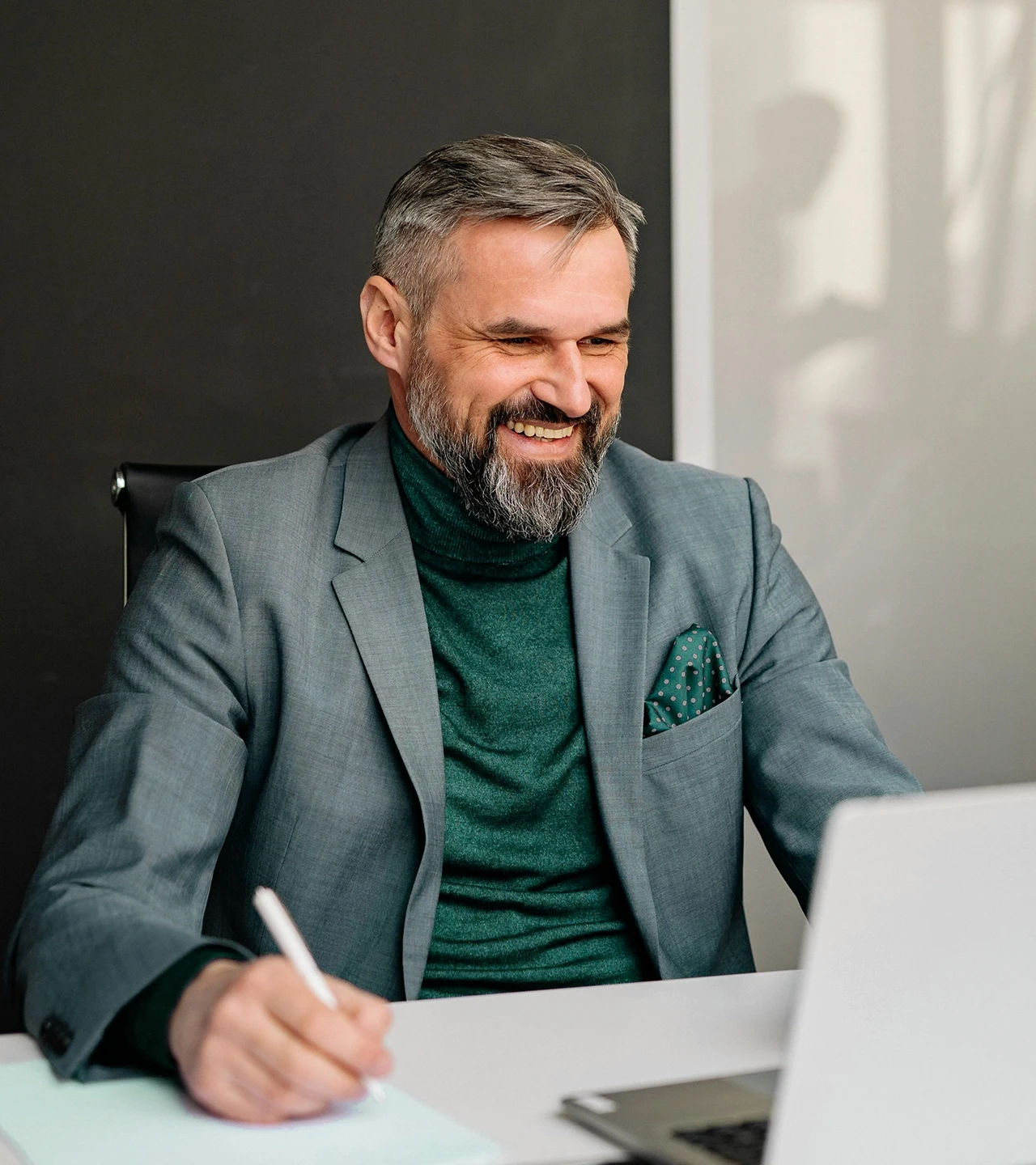 Homem grisalho sorrindo com caneta e notebook à sua frente