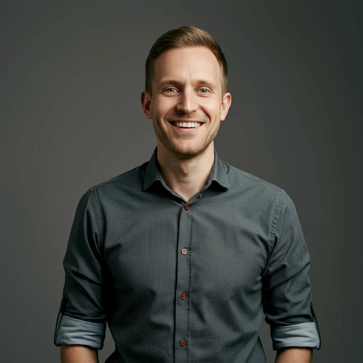 Friendly headshot of a smiling man wearing a button-down shirt against a dark grey wall.