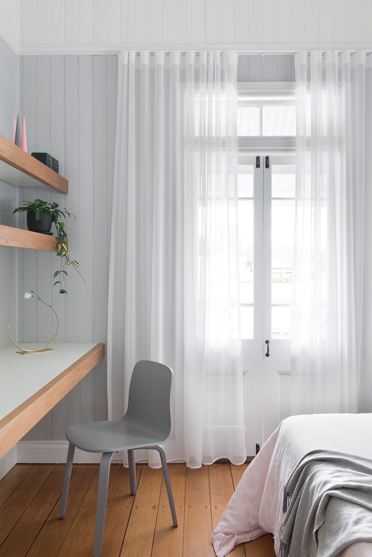 Light-filled bedroom with sheer curtains, built-in desk, and warm timber flooring under soft daylight