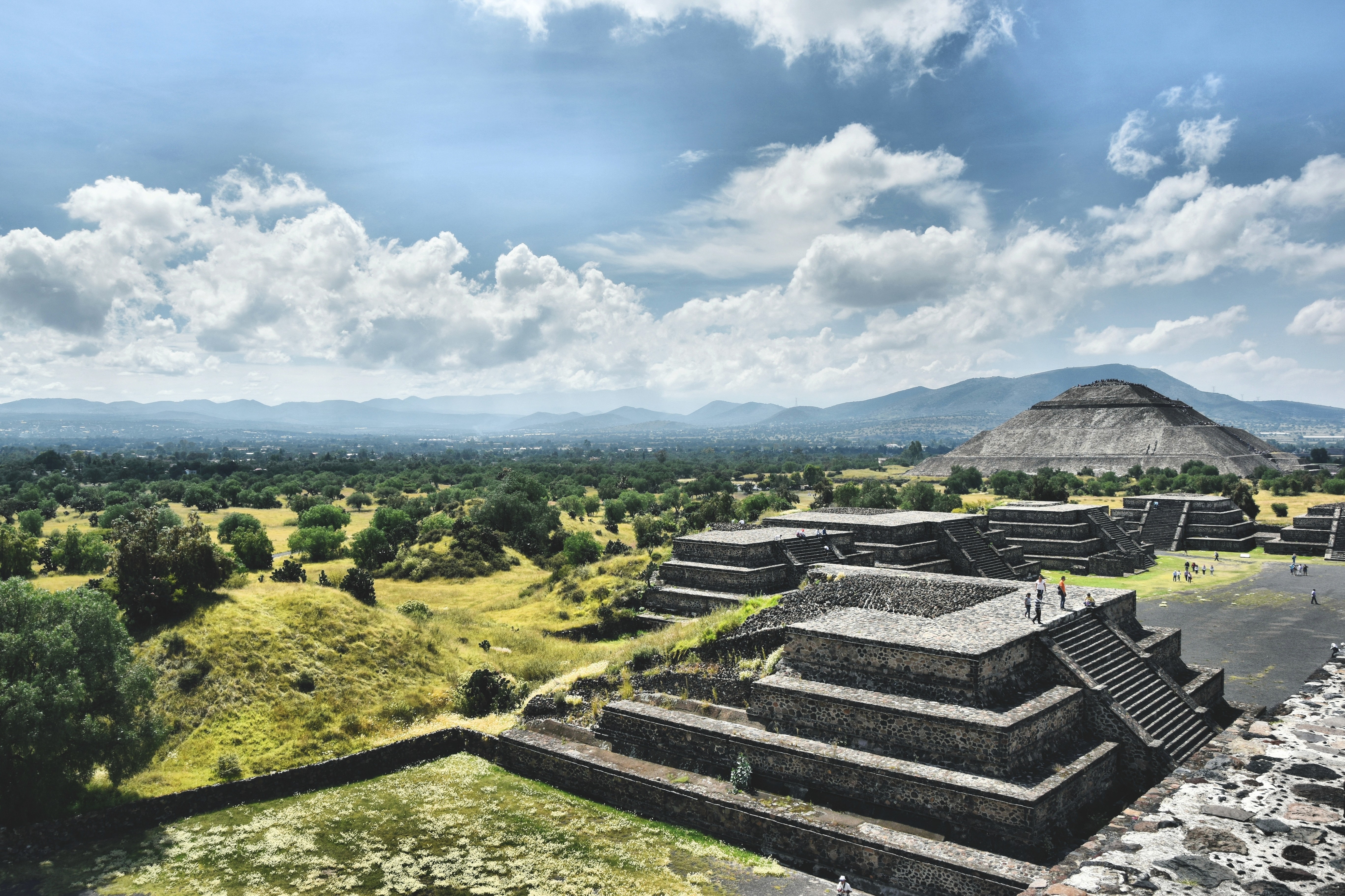 A wide, sweeping view of Monte Albán, Mexico, with people walking up the stepped pyramids