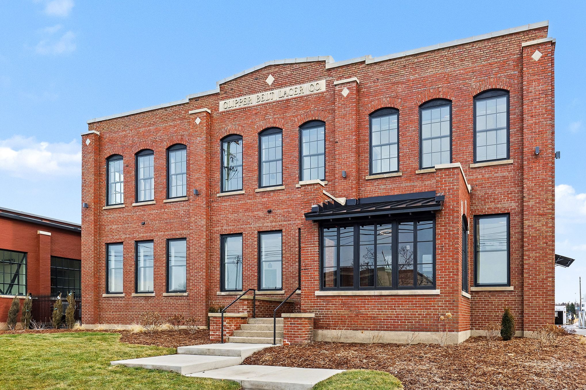 A large white building with a modern architectural design, featuring multiple windows and a clear blue sky in the background.