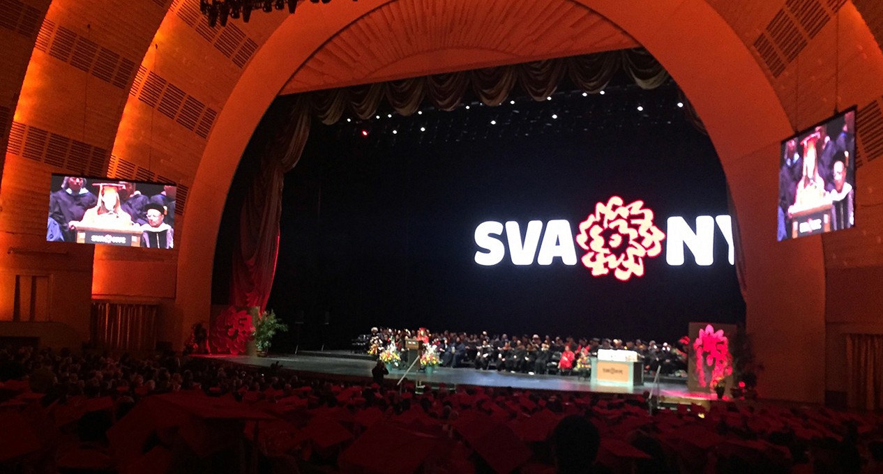 A photo of a theatre hall with some teachers and students on the scene. Also behind them there is the SVA NYC logo.