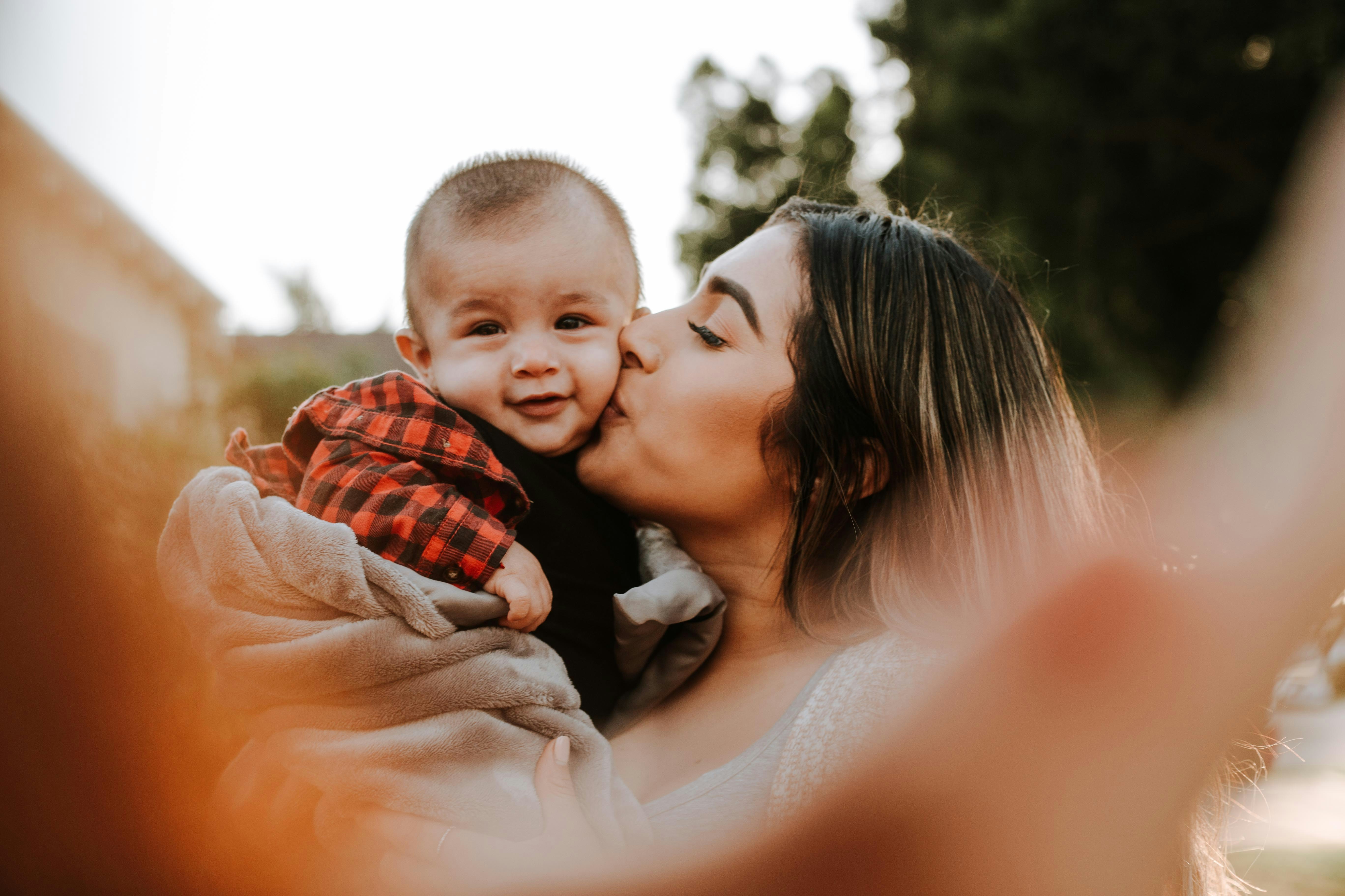 A woman holding his baby and kissing on the cheek