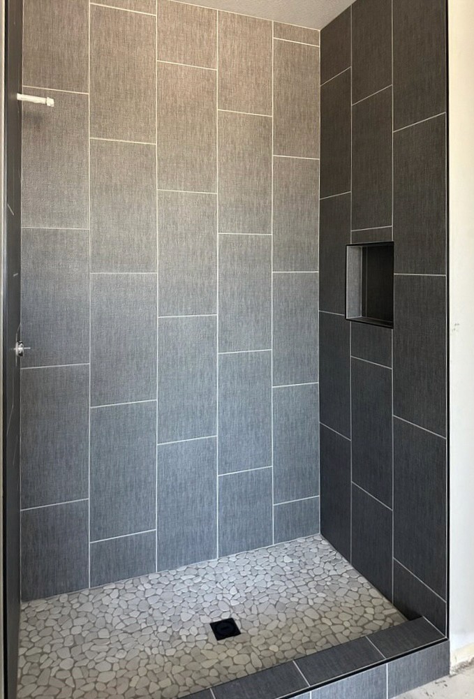 Contemporary shower featuring large dark grey rectangular wall tiles with a textured finish, a contrasting black built-in shower niche, and a light grey pebble mosaic shower floor.