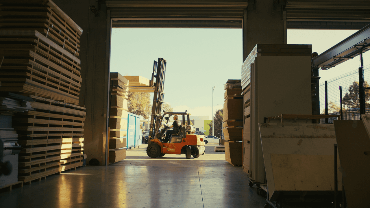 View down a warehouse aisle with shelves on both sides and natural light at the end
