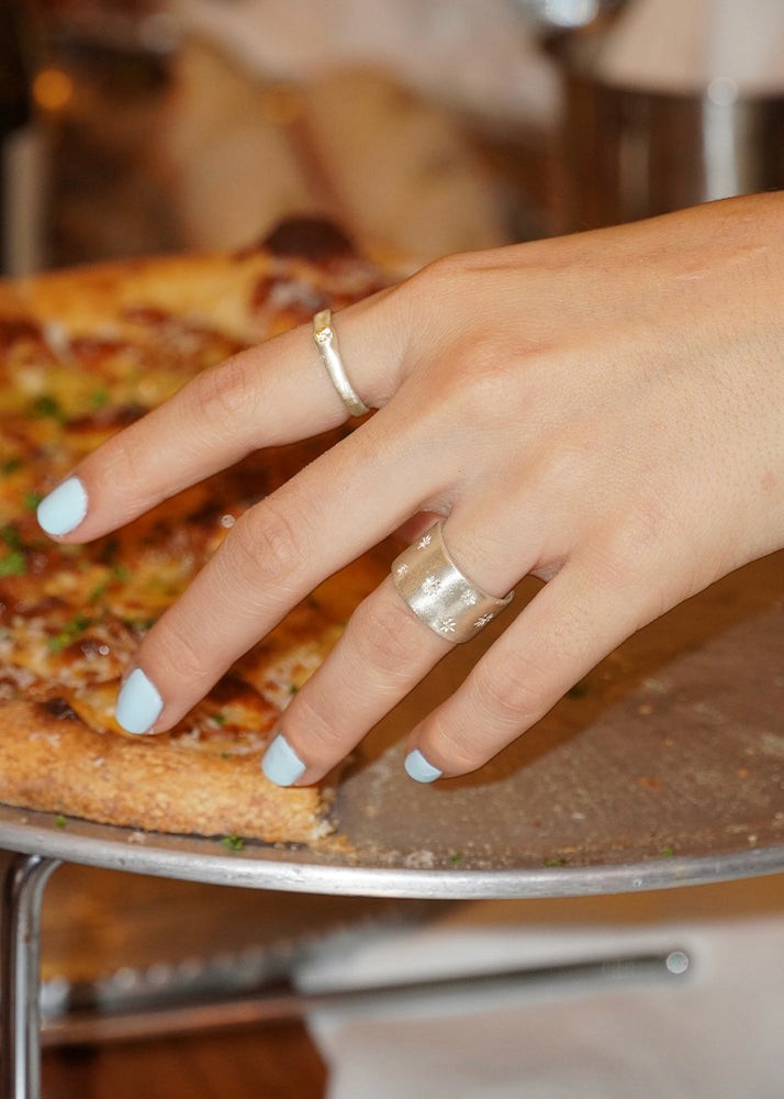 Hand with silver rings on a pizza, blurred background