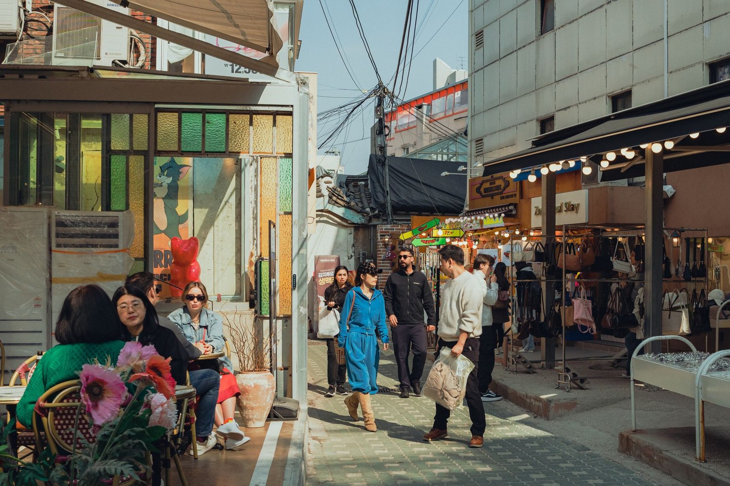 A busy shopping street in Seoul, shoppers moving between storefronts and cafes.