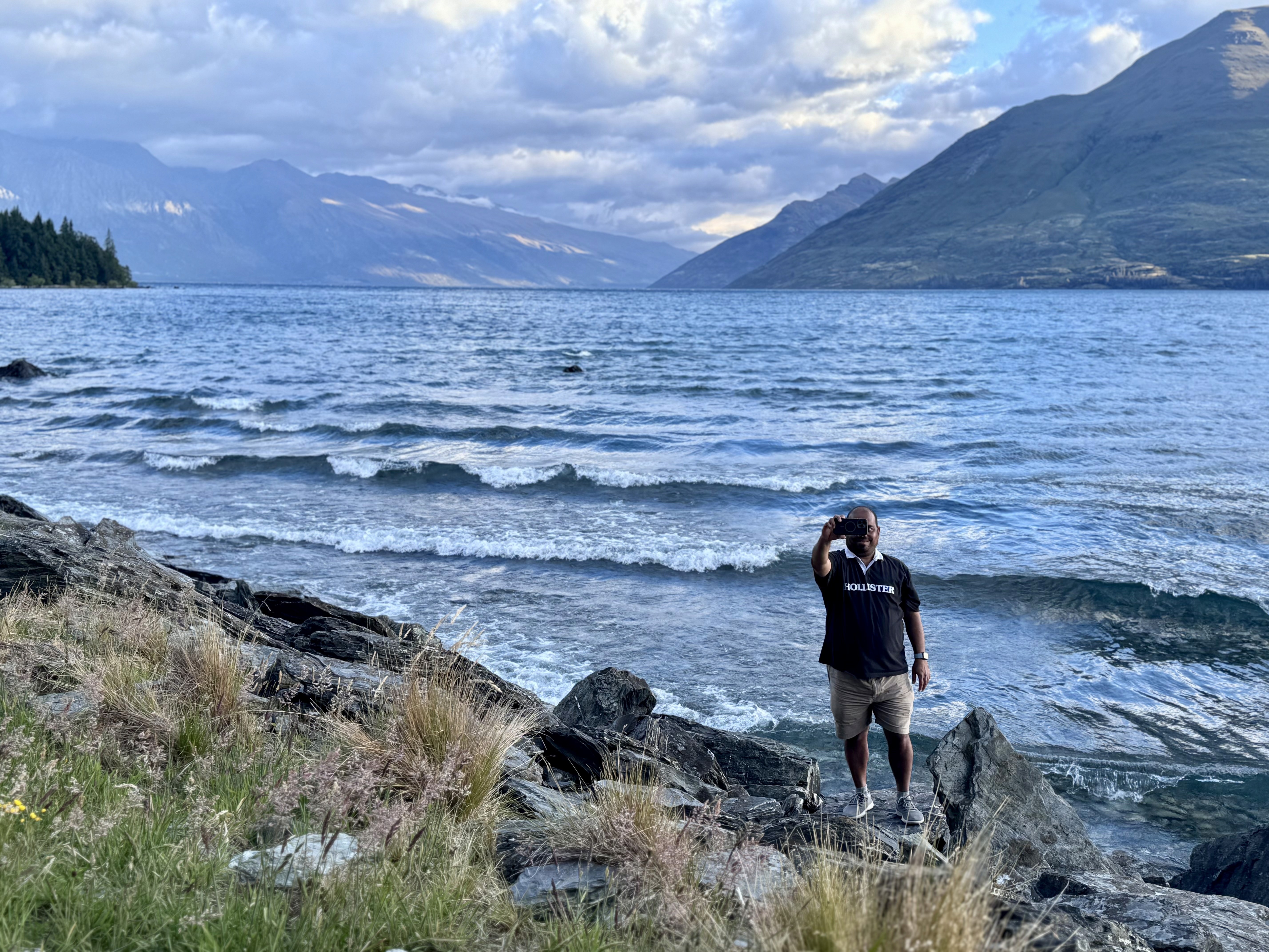 A man clicking a selfie by the shores of lake Wakatipu with the Remarkables in the background