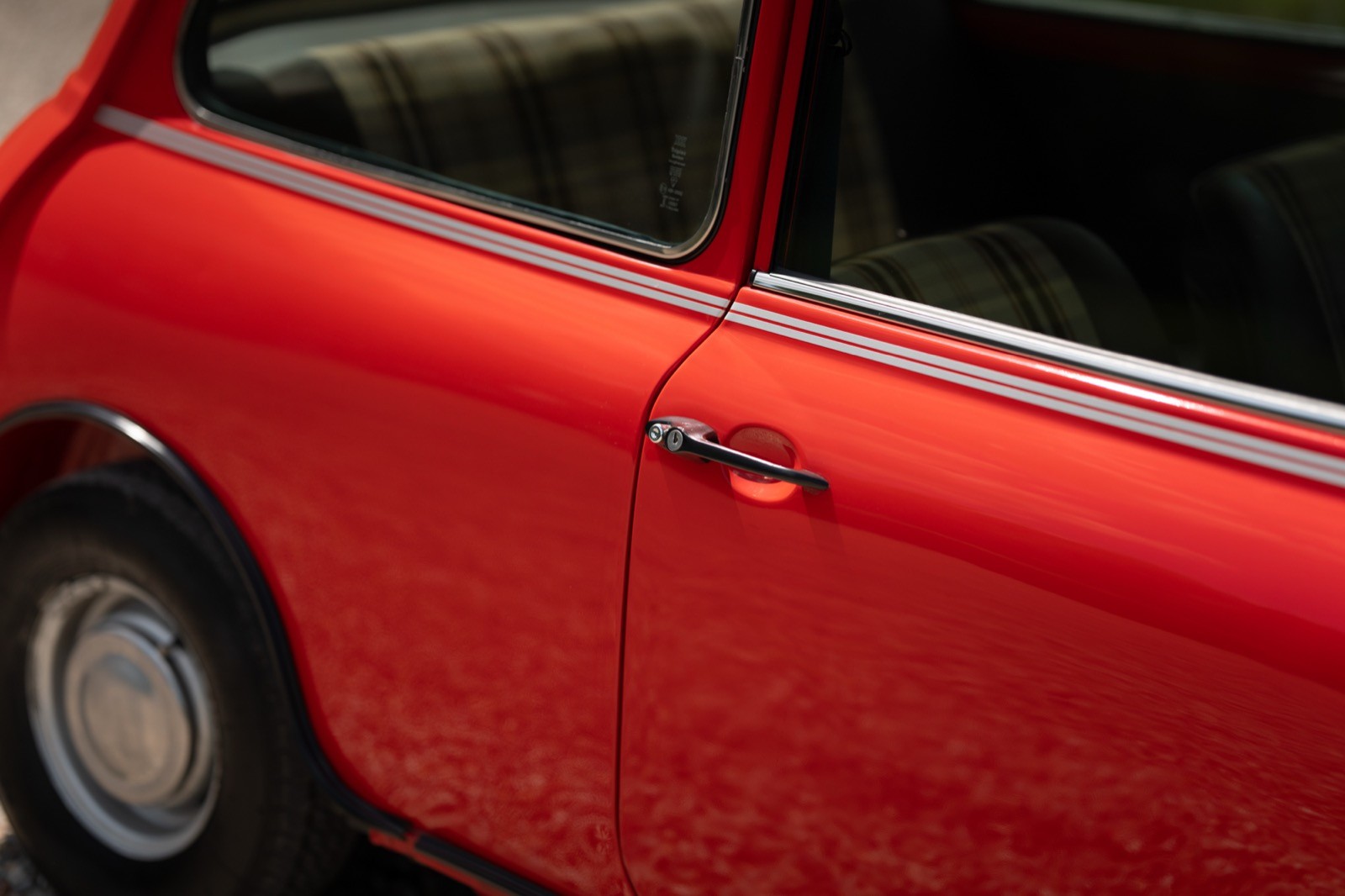 Close-up of a bright red car door with chrome accents and a rounded design.