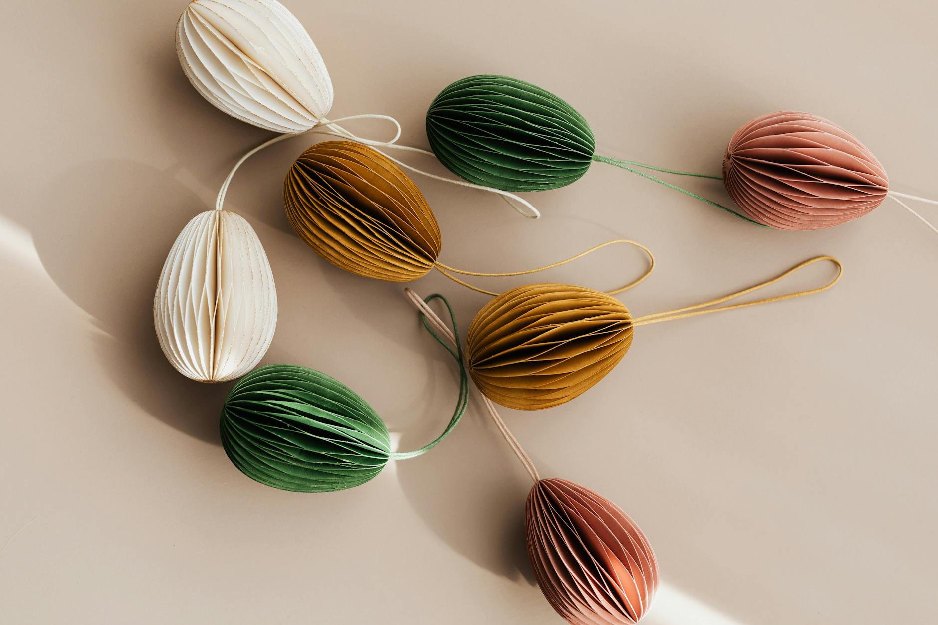 From above of pastel colorful crafts made of cardboard with thin cords for pendant souvenir scattered on beige table at sunny day