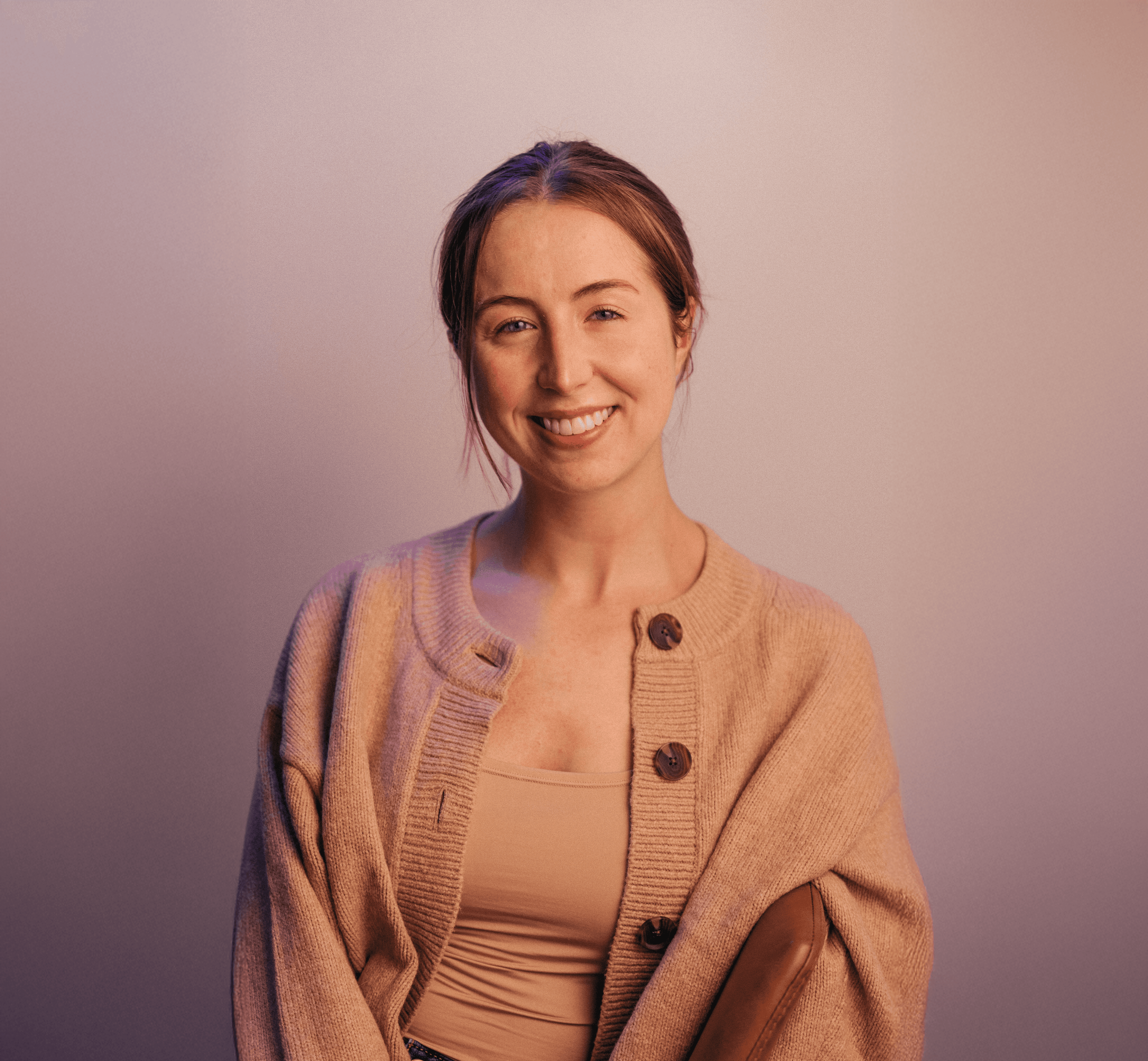 Allie Paschal with a tan sweater on in front of a plain wall