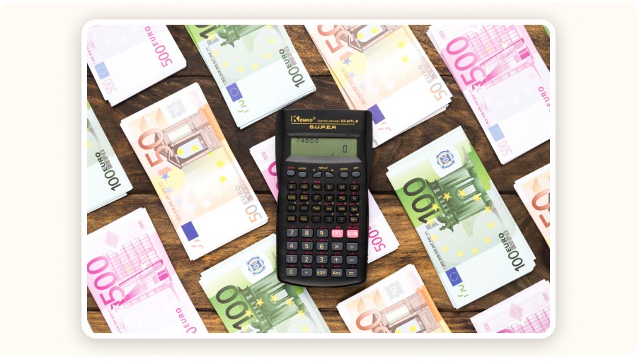 Calculatrice posée au centre d’une table en bois, entourée de piles de billets en euros