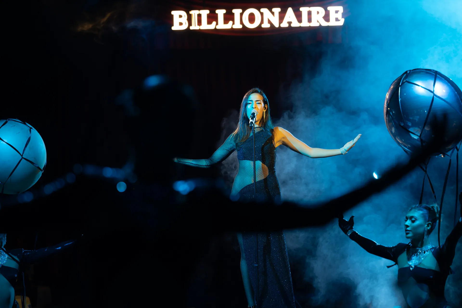 Singer performing under the illuminated Billionaire sign in blue haze at Billionaire Dubai
