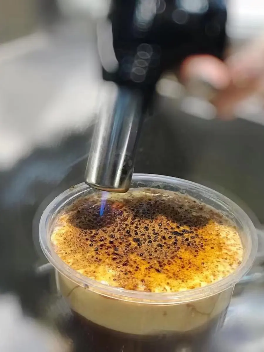  A close-up of a bruleed topping being torched, creating a caramelized finish on a signature Cozy Tea Loft drink, showcasing their craftsmanship and attention to detail.