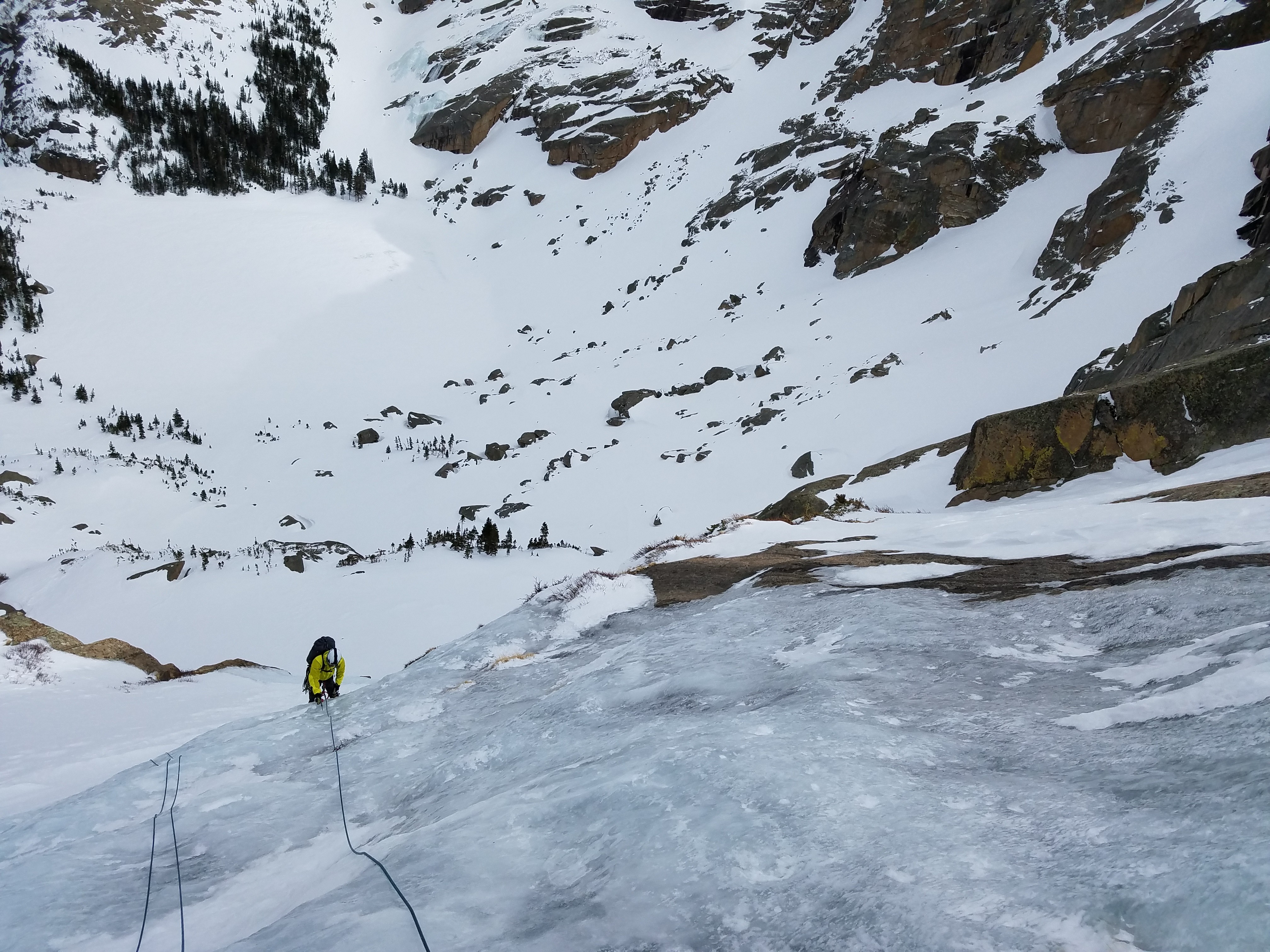 Climber ascends ice slab high above alpine lake in Rocky Mountain National Park