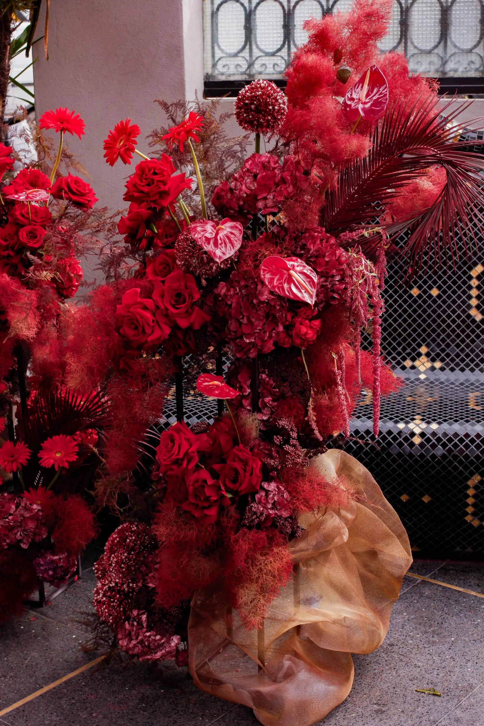 Arreglo de piso con rosas, anturios y follaje bordó sobre base de tul dorado.