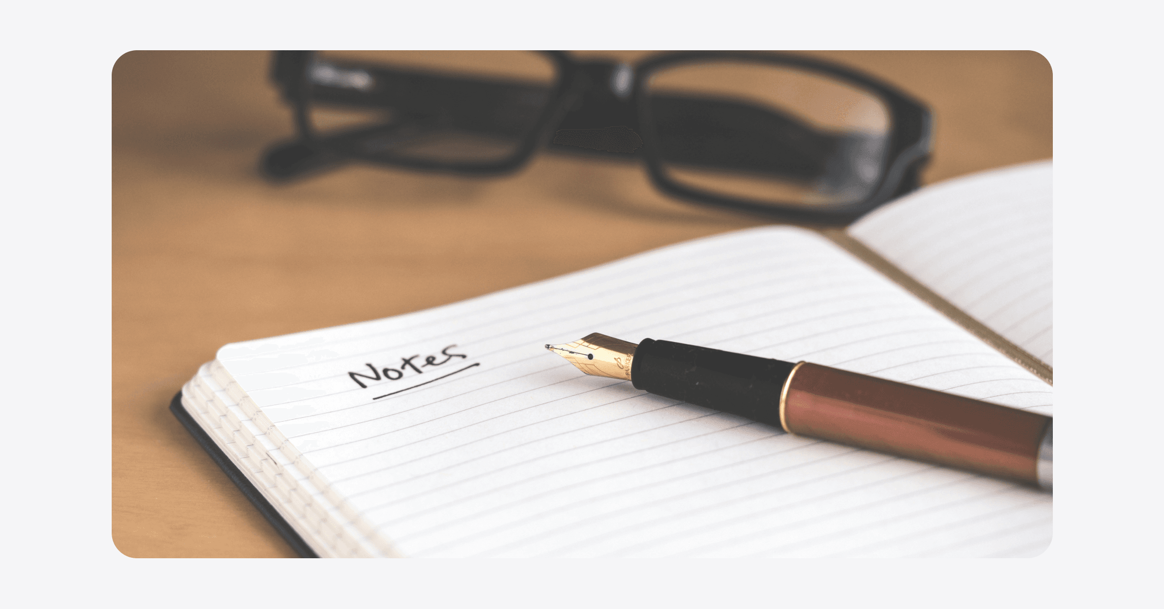 Image showing a fountain pen on a notebook and glasses in the background